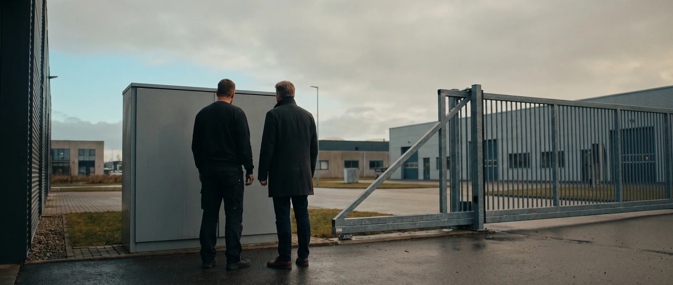 An installer and a customer talking beside an outdoor cabinet by a gate