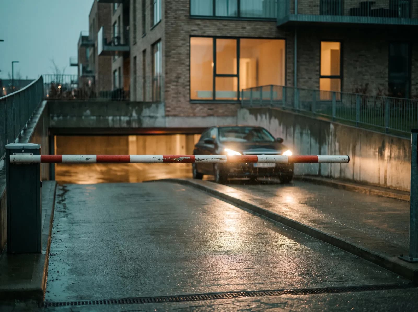 En parkeringsbom ved en boligejendom, hvor en bil venter